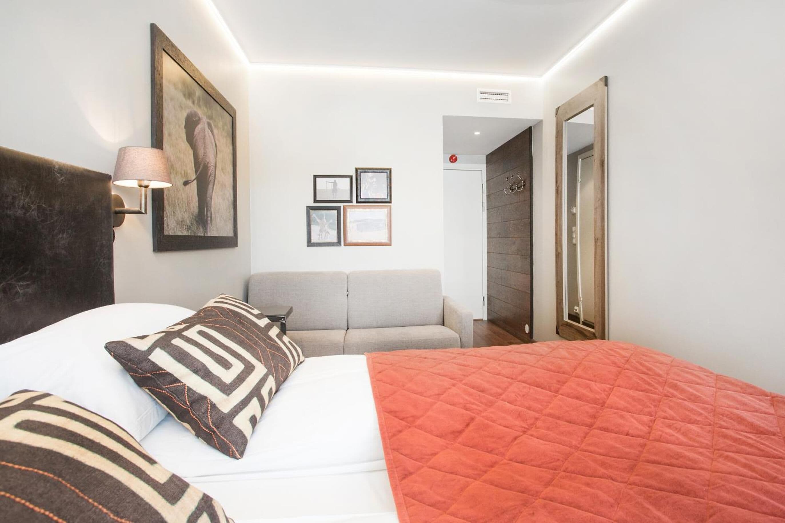 A bedroom with a bed, a sofa, a painting, and framed pictures on the wall.