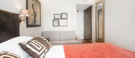 A bedroom with a bed, a sofa, a painting, and framed pictures on the wall.