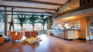 A spacious lobby with a wooden floor, a giraffe sculpture, a bar area, and a seating area with orange chairs. - Dyreparken Safarihotell (Kristiansand)