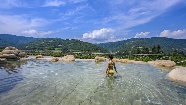 Una piscina cristalina con valla de madera y rocas, rodeada de colinas verdes.