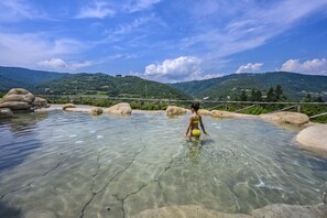 A clear pool with a wooden fence and rocks, surrounded by green hills. - Tenuta Pian D'Attesio (Castelletto Uzzone)
