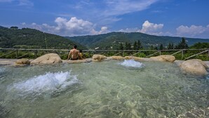Un cuerpo de agua cristalina con rocas, un puente de madera y un paisaje montañoso al fondo.