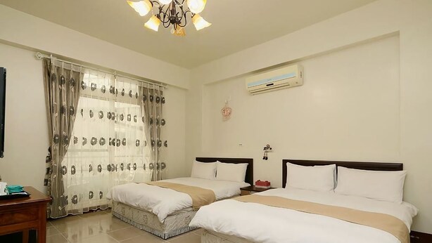 A hotel room with two beds, a desk, a chandelier, an air conditioner, and a window with curtains. - Leisure Homestay (Hualien City)