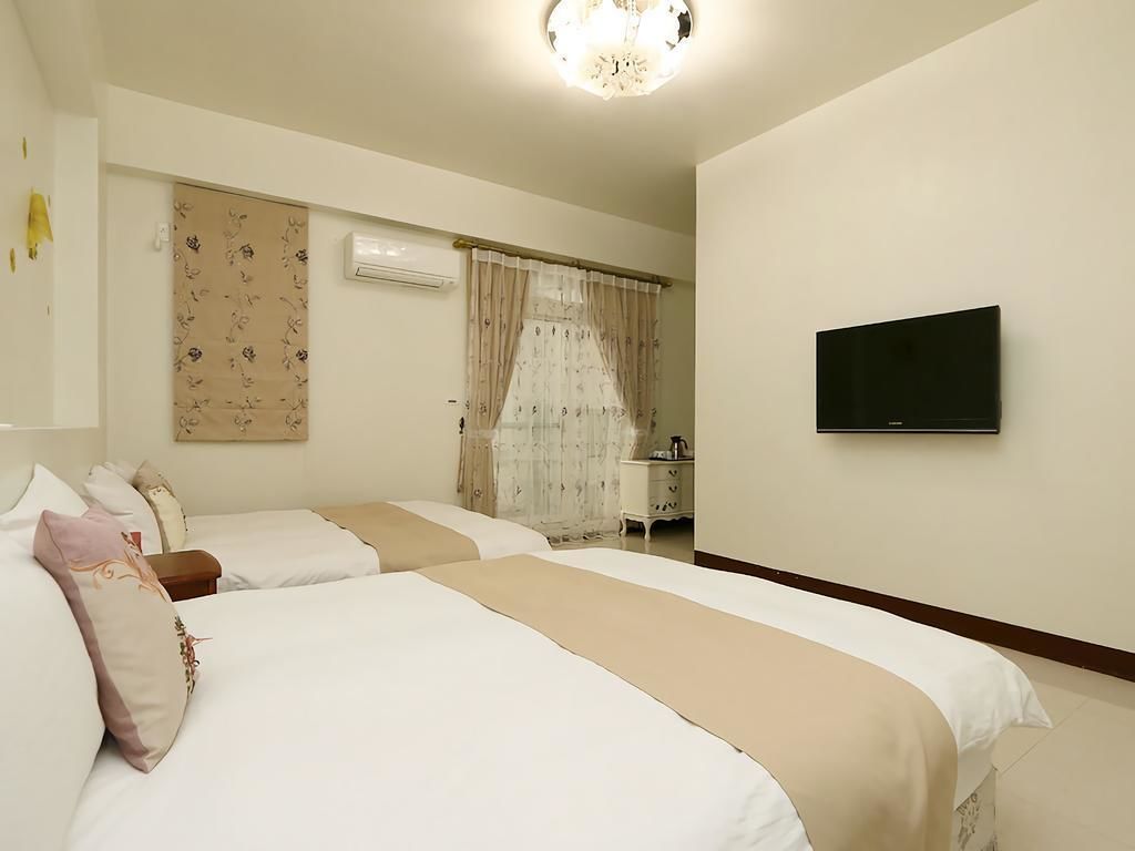 Habitación de hotel con dos camas, un televisor en la pared y una ventana con cortinas.