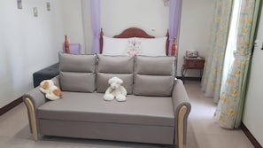 A bedroom with a grey sofa, two pillows, a small bedside table, and a nightstand. - Leisure Homestay (Hualien City)