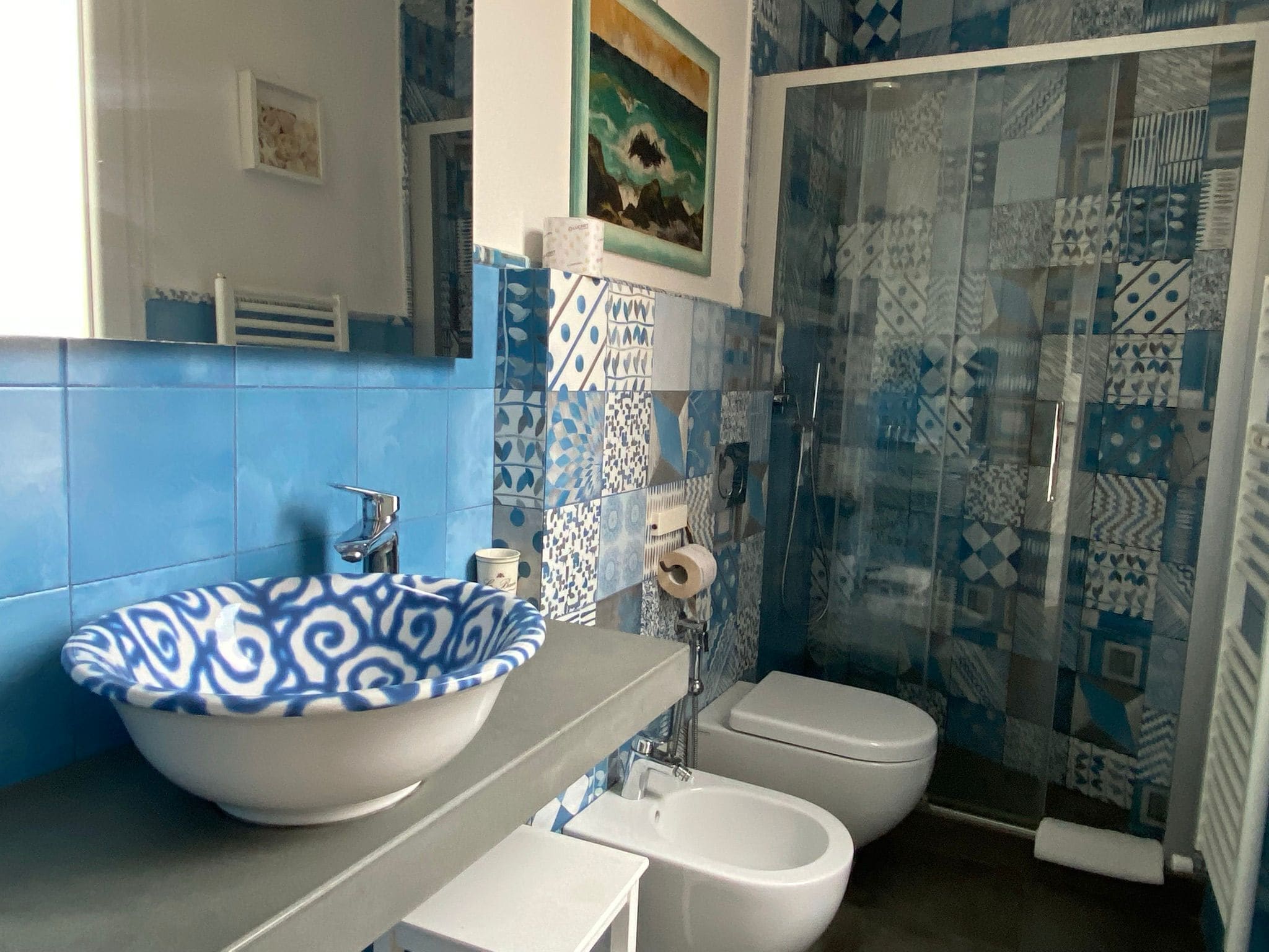 Une salle de bain avec un lavabo aux motifs bleus et blancs, des toilettes et une douche dont les carreaux sont également à motifs.