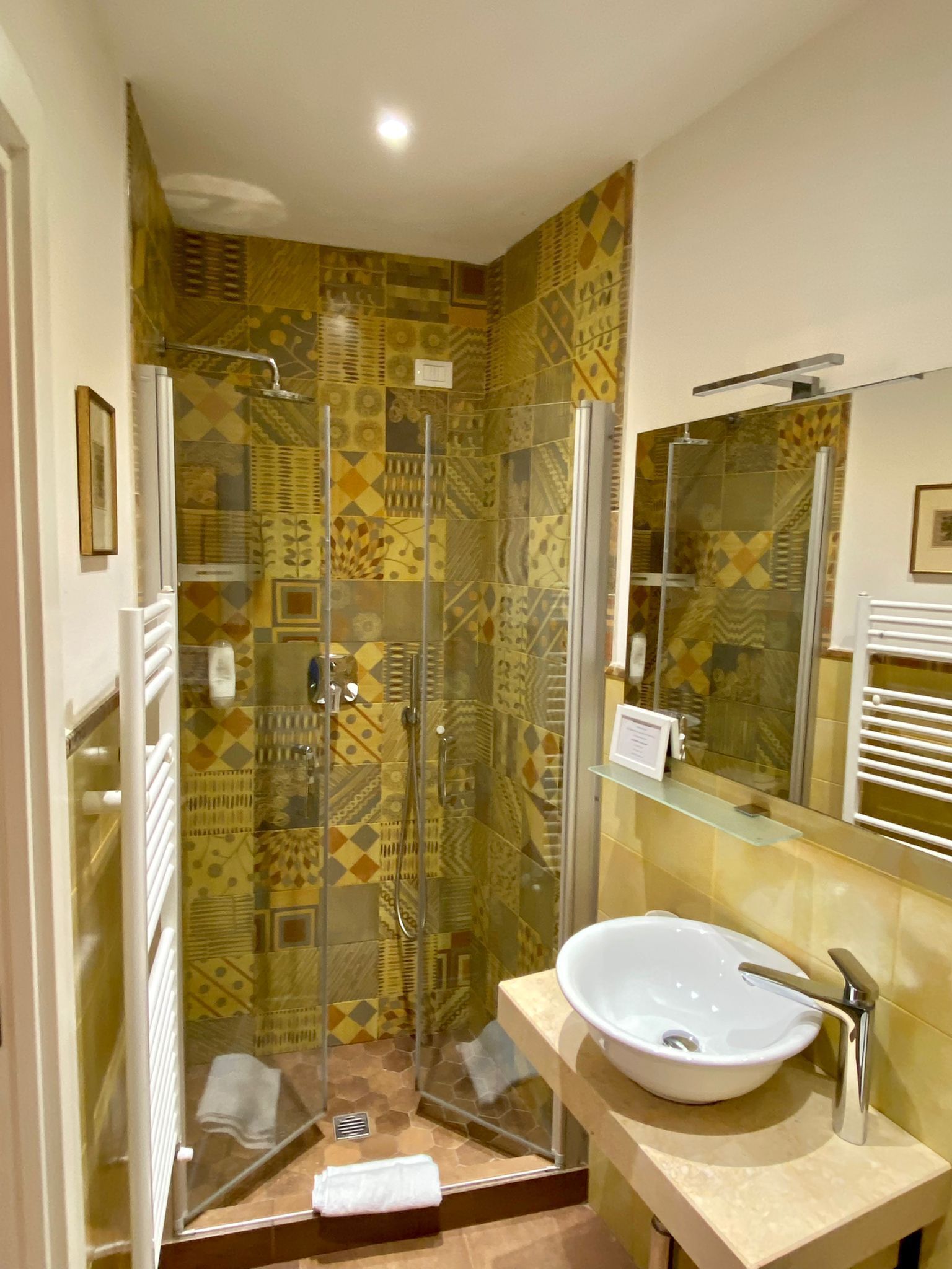 Un baño con ducha envuelta en vidrio, lavamanos con espejo y azulejos decorativos.