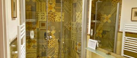 Un baño con ducha envuelta en vidrio, lavamanos con espejo y azulejos decorativos.