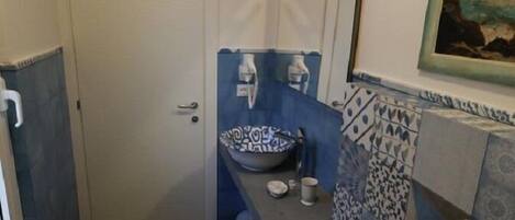 Ein kleines Badezimmer mit einer weißen Tür, einem Waschbecken mit blauem Muster, einem kleinen Hocker und einer Toilette.
