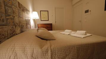 A neatly made bed with a quilted cover, a wooden headboard, and two neatly folded towels on the bed.