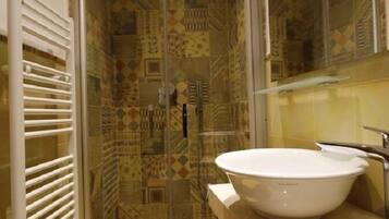 Ein Badezimmer mit einer gläsernen Duschkabine, einem weißen Waschbecken und gemusterten Fliesen.
