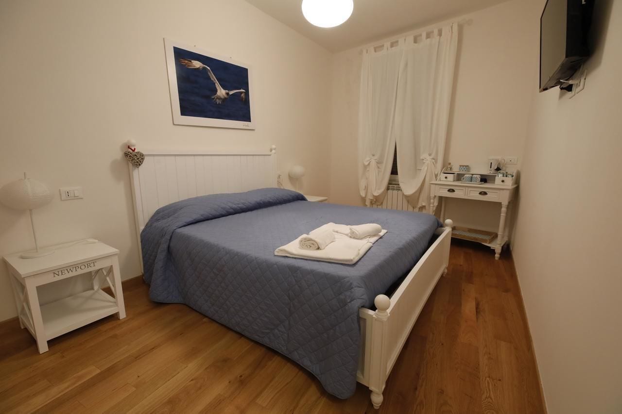 Una camera da letto con un letto, un comodino, una scrivania, una cassettiera, uno specchio e un quadro appeso al muro.