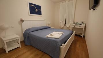 A bedroom with a bed, a bedside table, a nightstand, a dresser, a mirror, and a painting on the wall.