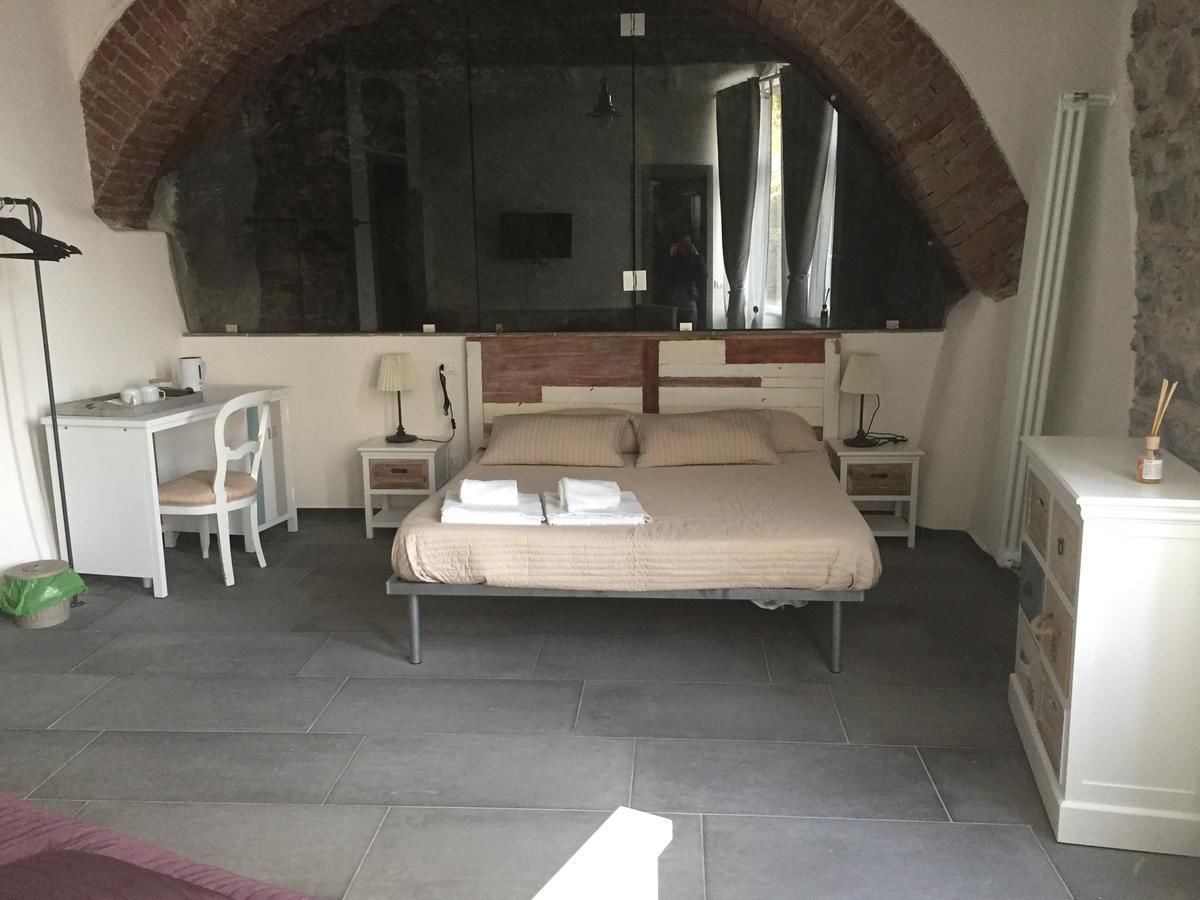 A bedroom with a bed, a desk, a chair, a dresser, and a large arched window.