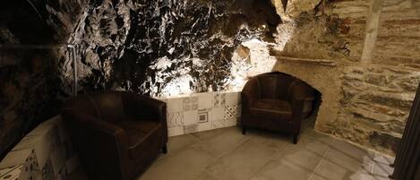 A room with a cave-like interior, featuring two leather chairs, a tiled floor, and a wall with a mosaic pattern.