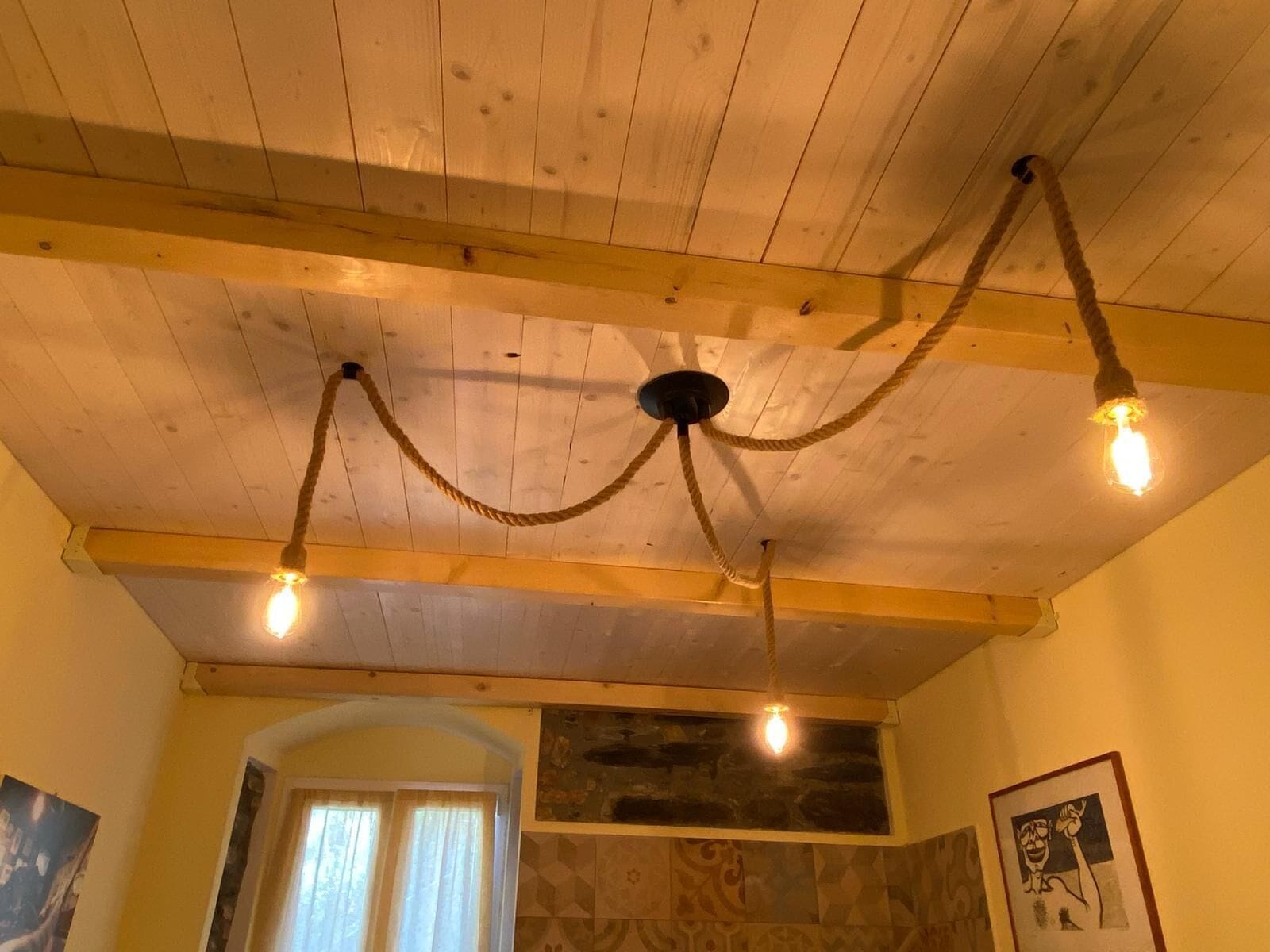 A room with a wooden ceiling, exposed beams, and a rustic chandelier with three bulbs.