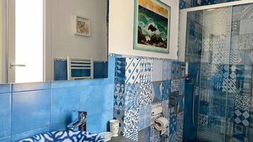 A bathroom with blue and white patterned tiles, a sink, a toilet, a shower with glass doors, and a framed painting on the wall.