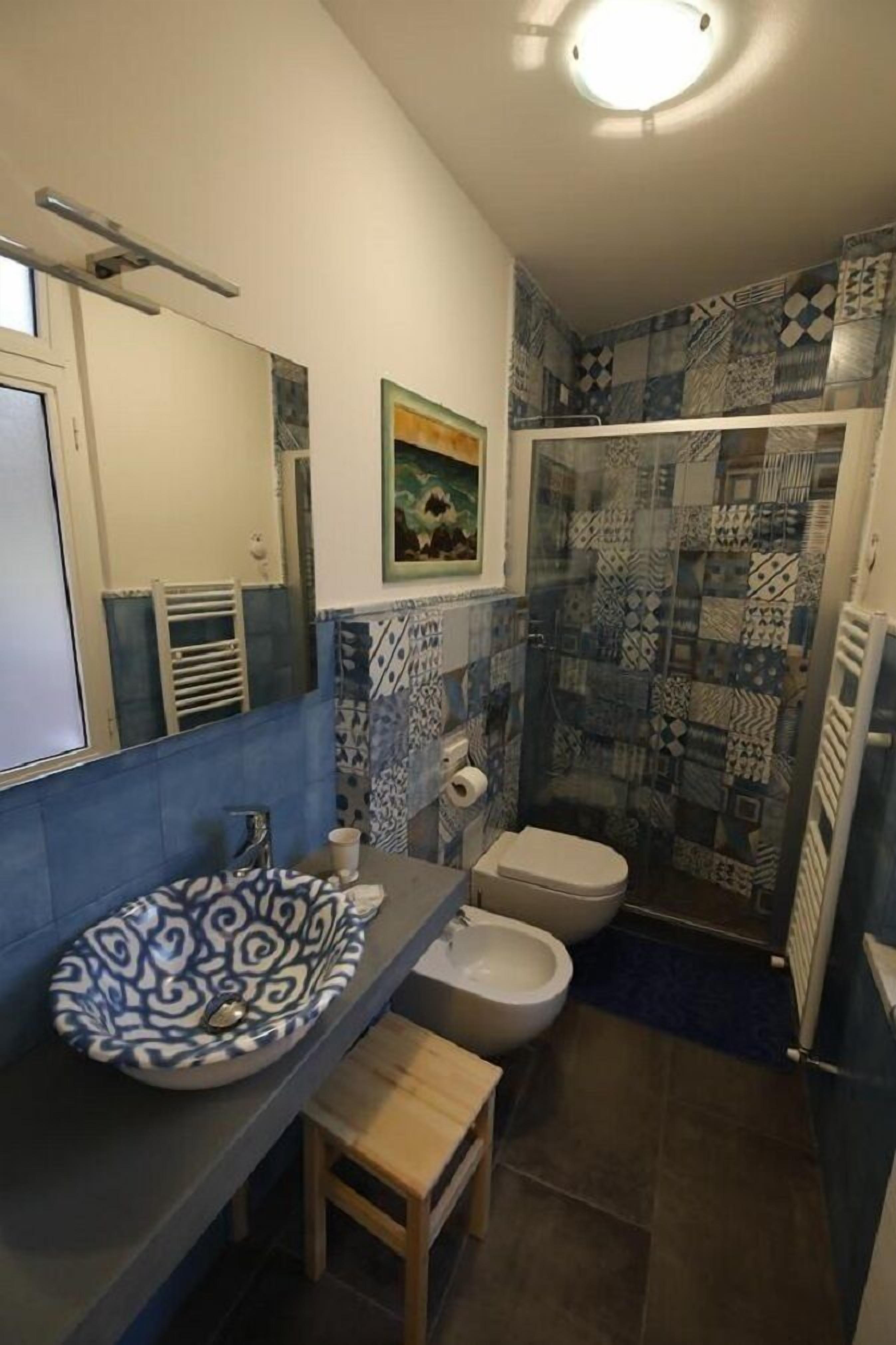 A bathroom with a blue and white patterned tile backsplash, a sink with a blue and white bowl, a toilet, and a shower with a similar tile pattern.