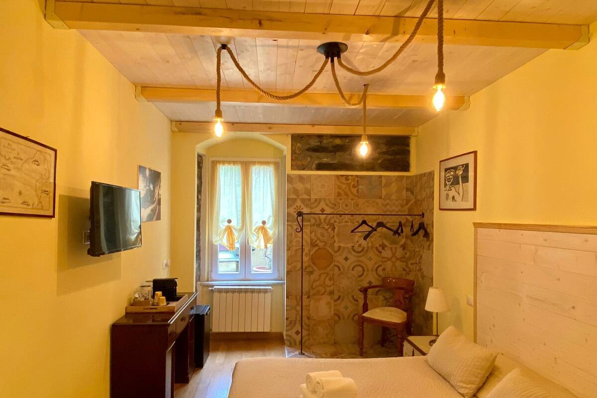 Una habitación de hotel con una cama, mesita de noche, lámpara y televisión en la pared.