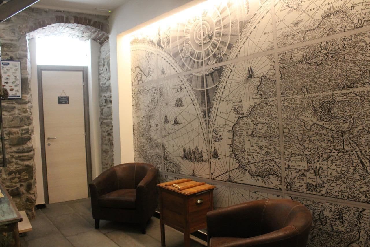 Une pièce avec une grande carte murale, deux fauteuils en cuir, une table d’appoint en bois et un mur en pierre.