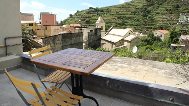 Una terraza con mesa y sillas, con vistas a una colina con campos en bancales y edificios.