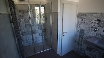 Casa de banho com azulejos estampados, cabine de duche em vidro e porta branca.