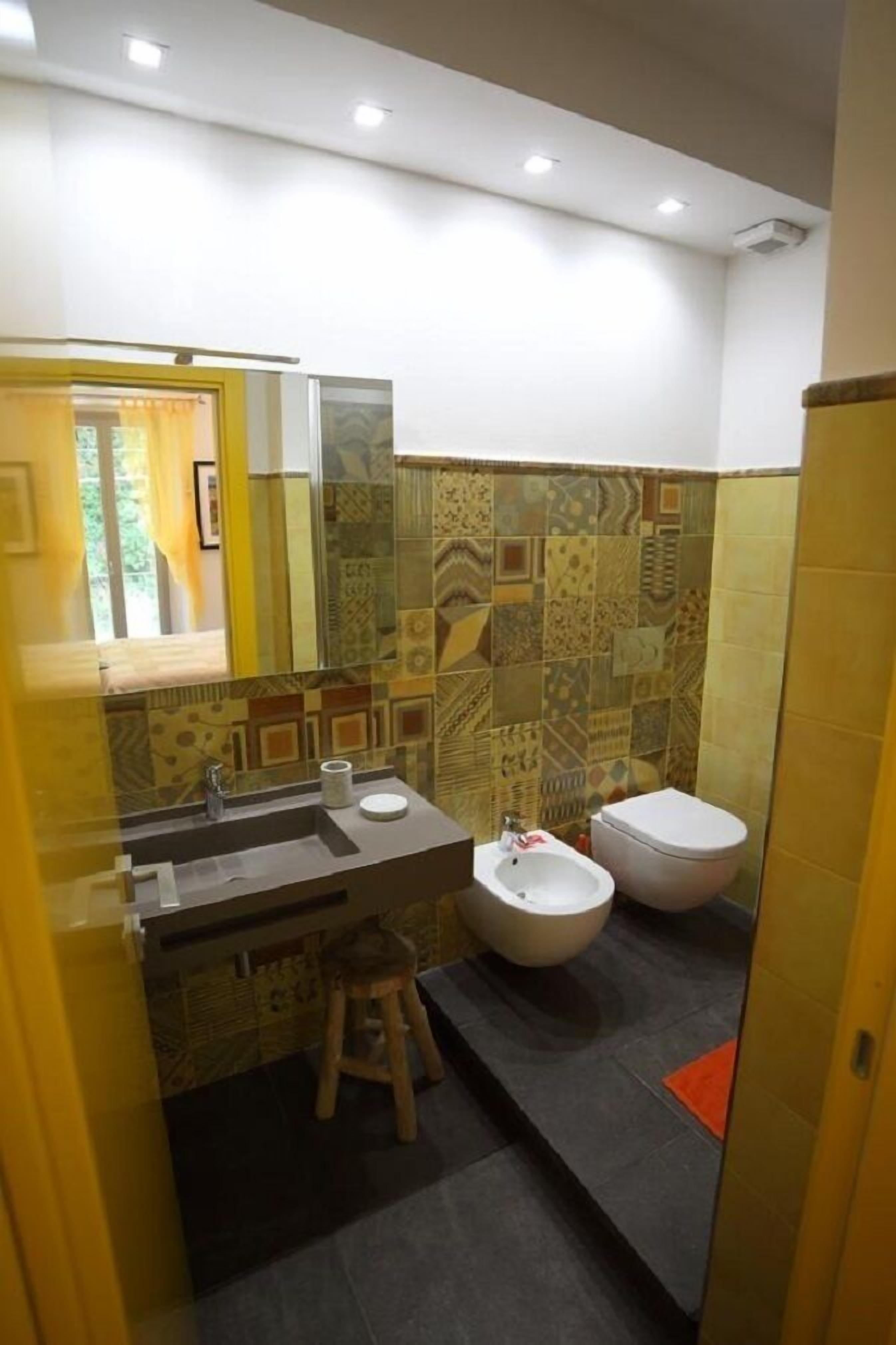 A bathroom with a patterned tile backsplash, a sink with a mirror, a bidet, and a toilet.