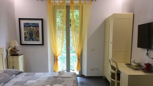 Un dormitorio con cama, escritorio, silla, armario, televisor y ventana con cortinas.