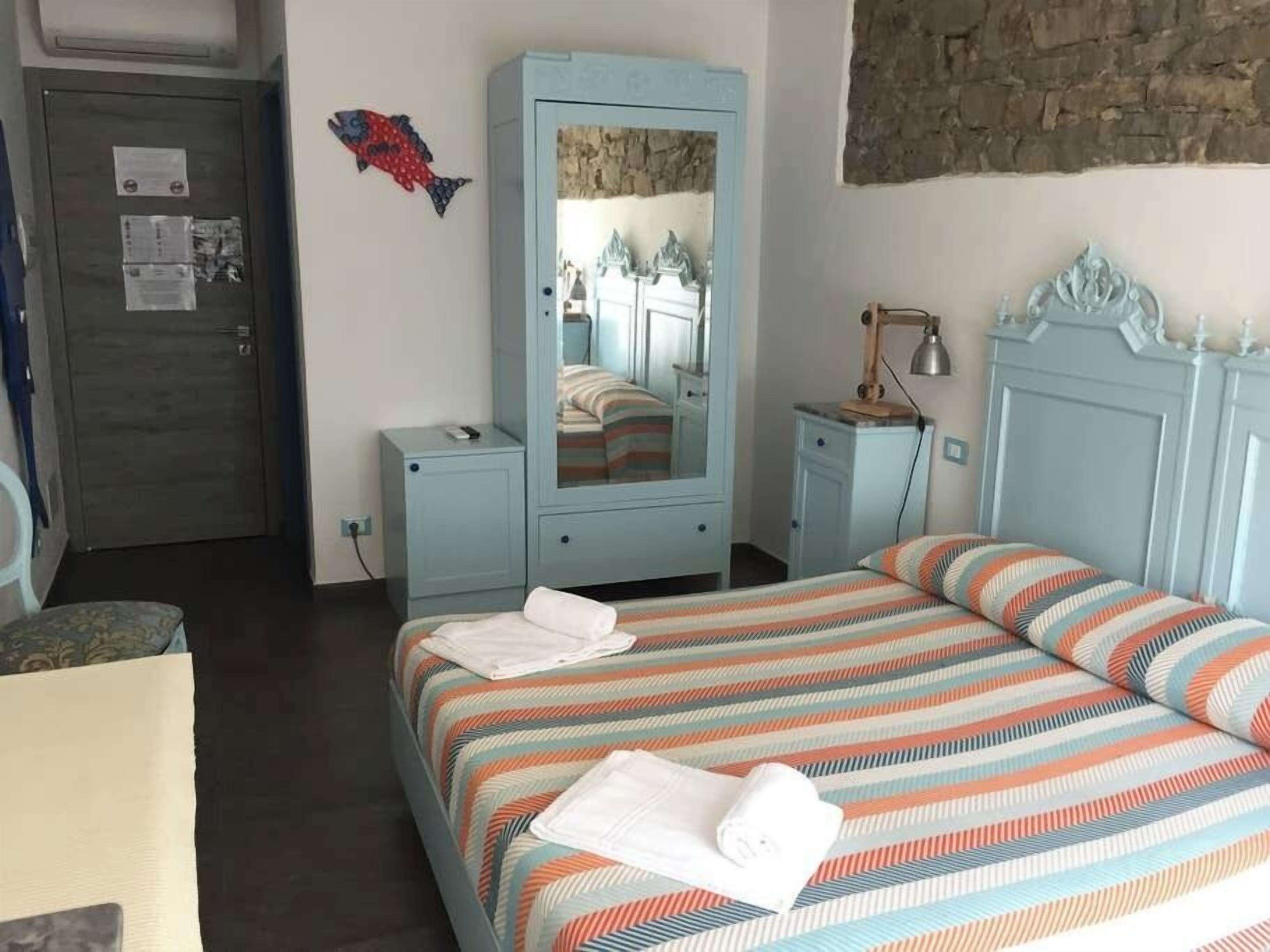 A bedroom with a bed, a wardrobe, a mirror, a lamp, and a fish decoration on the wall.