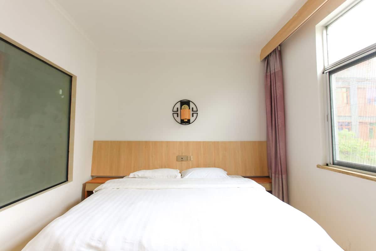 Una habitación de hotel con cama, un ventanal grande y una lámpara fijada a la pared.