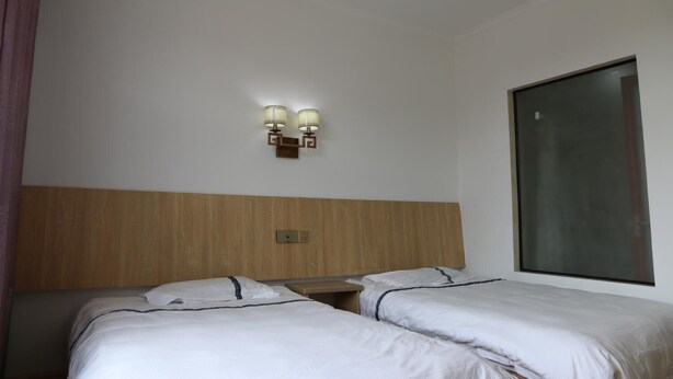 A hotel room with two single beds, a wooden headboard, a wall-mounted light fixture, and a large window. - Wuyishan City Chun Hui Traders Hotel (Nanping)