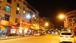A street at night with buildings, shops, and parked cars. - Wuyishan City Chun Hui Traders Hotel (Nanping)