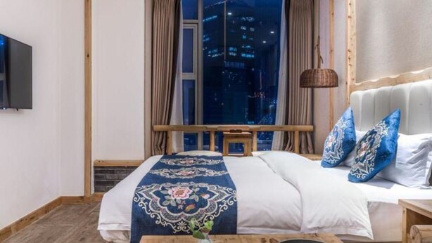 A hotel room with a bed, a wooden table with bowls, a TV on the wall, and a window with a city view. - Floral Hotel Qingshe Chengdu (Chengdu)