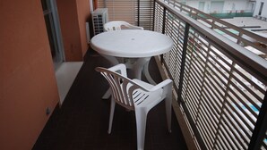 A balcony with a round table and two chairs, a railing, and a view of a building with multiple windows. - Casamare (Lignano Sabbiadoro)