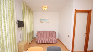 A room with a striped sofa, a television, a painting, and a door. - Casamare (Lignano Sabbiadoro)