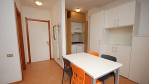 A compact kitchen with white cabinets, a white countertop, and a dining table with two chairs. - Casamare (Lignano Sabbiadoro)