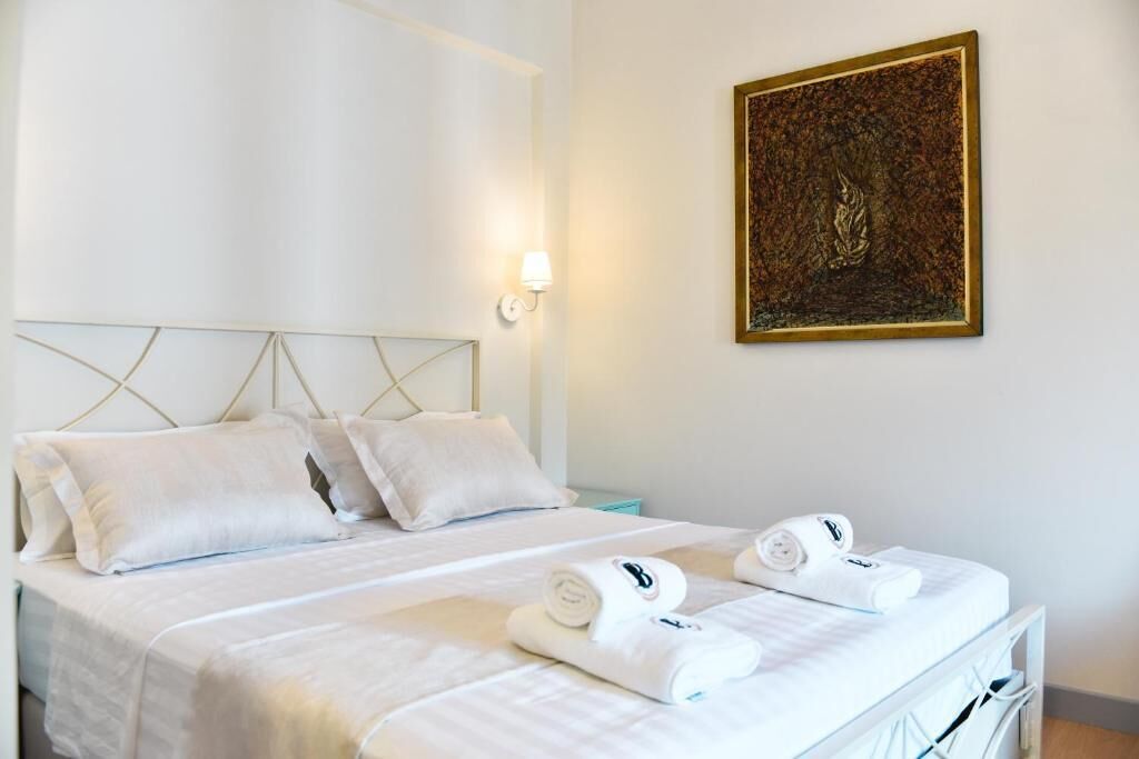 Une chambre d’hôtel comprenant un lit, des oreillers, une table de chevet, une lampe fixée au mur et un tableau encadré.