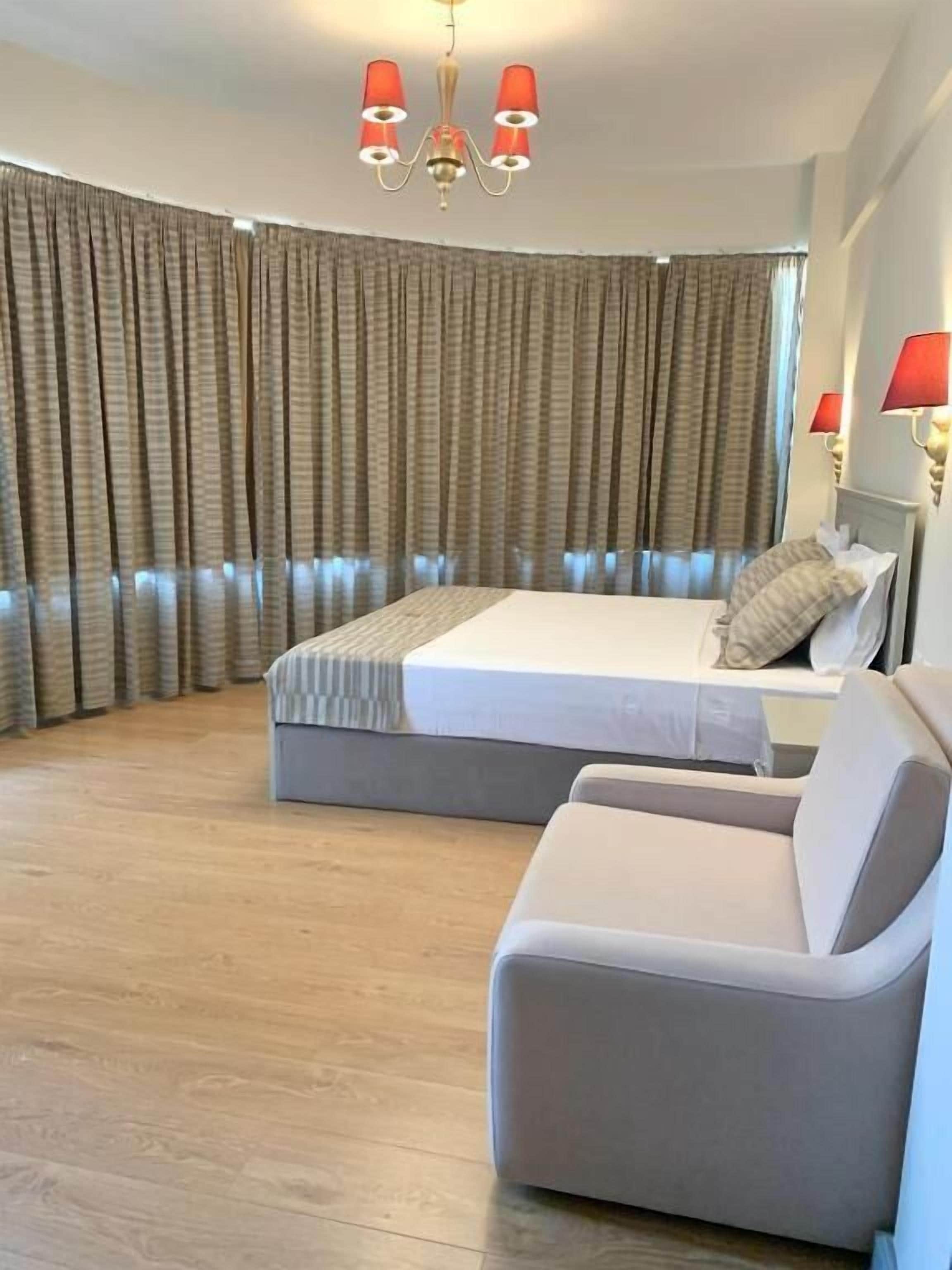 Una habitación de hotel moderna con una cama grande, un sofá, suelo de madera y un candelabro.