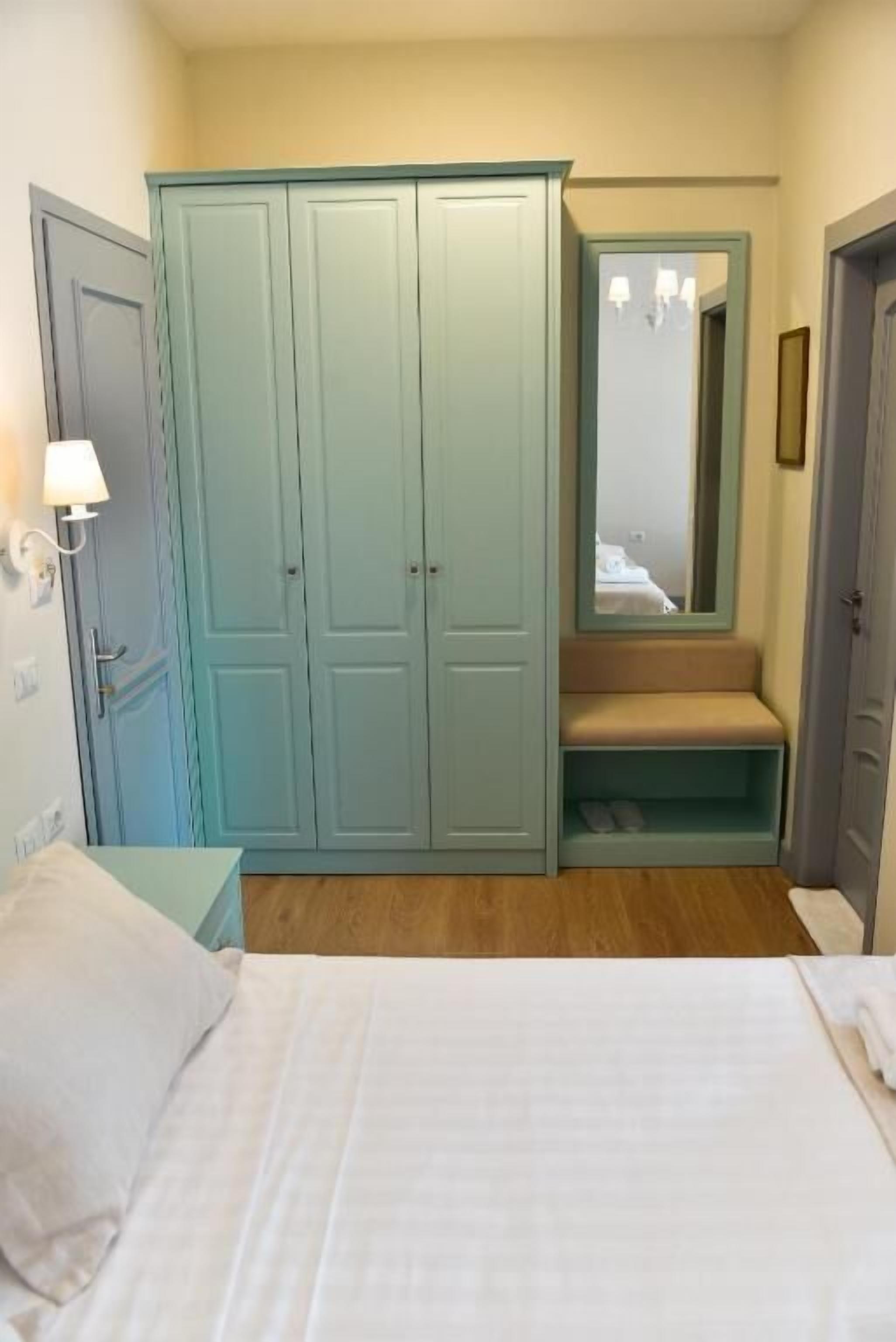 A bedroom with a bed, a wardrobe, a bench, and a mirror.