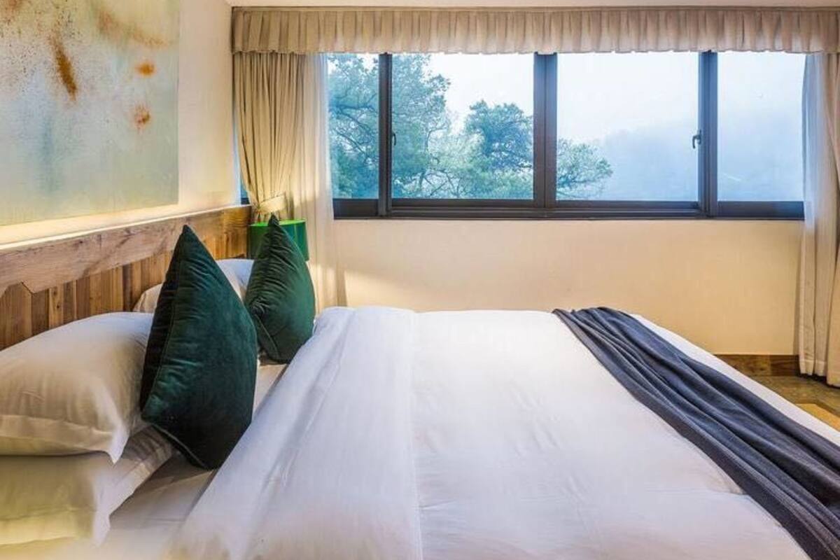 Ein Hotelzimmer mit einem großen Bett, zwei Kissen, einem Fenster mit Blick auf Bäume und einem Holzkopfschild.