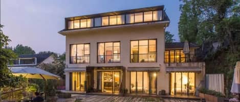 Une maison moderne à deux étages, dotée de grandes fenêtres et d’un espace extérieur aménagé avec un coin salon couvert.