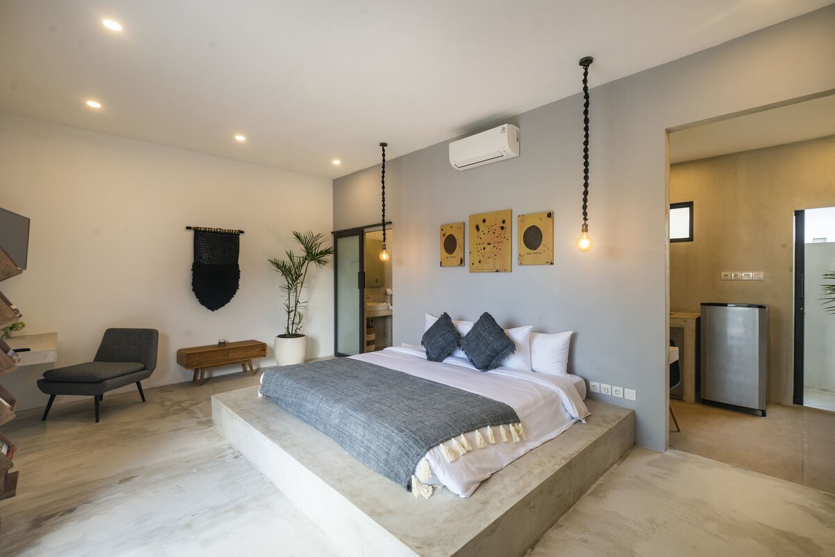 A modern bedroom with a large bed, a chair, a bedside table, and a potted plant.
