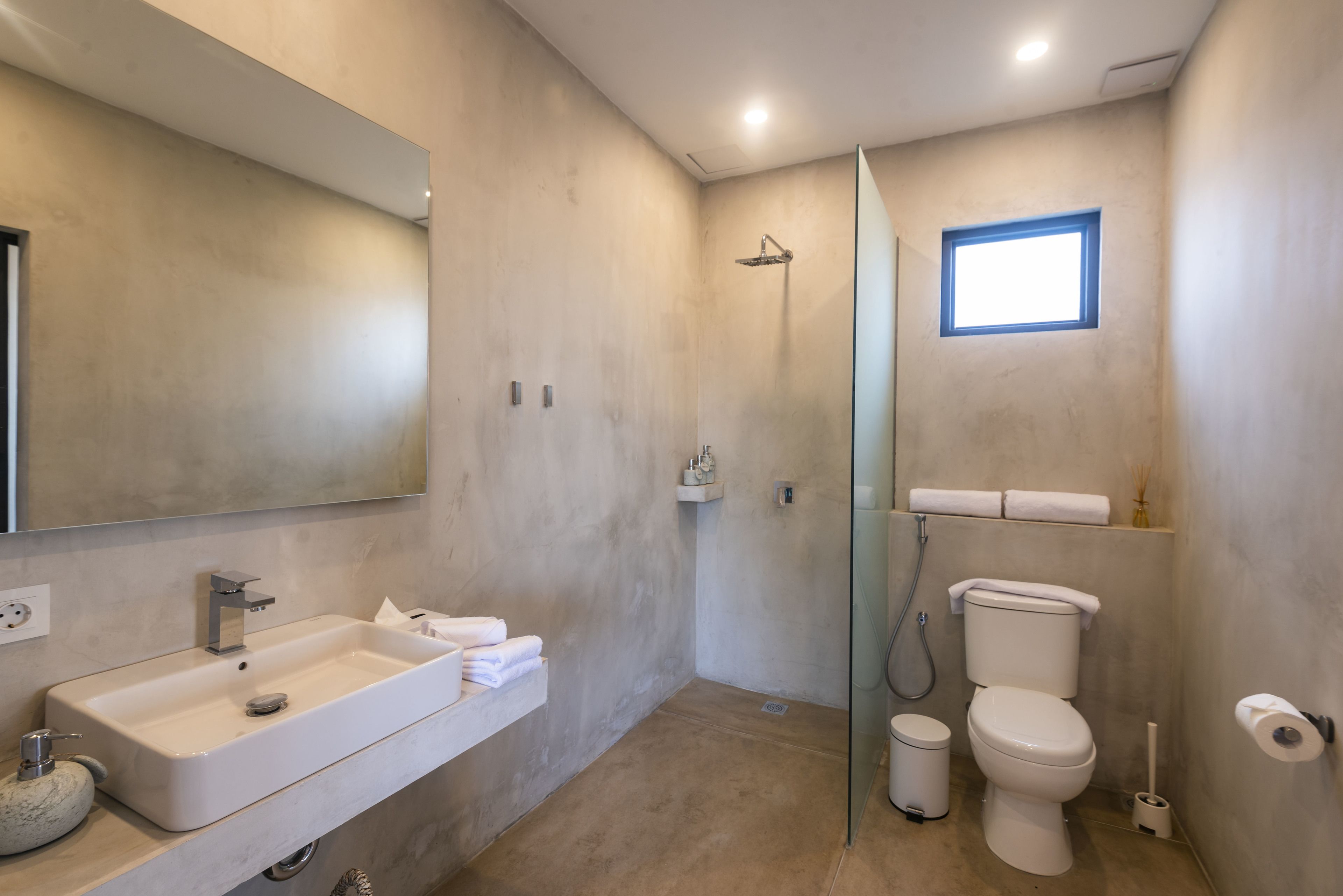 Egy modern fürőszoba, amelyben egy nagy tükör, egy mosdókagyló, egy WC és egy zuhanyzó található.