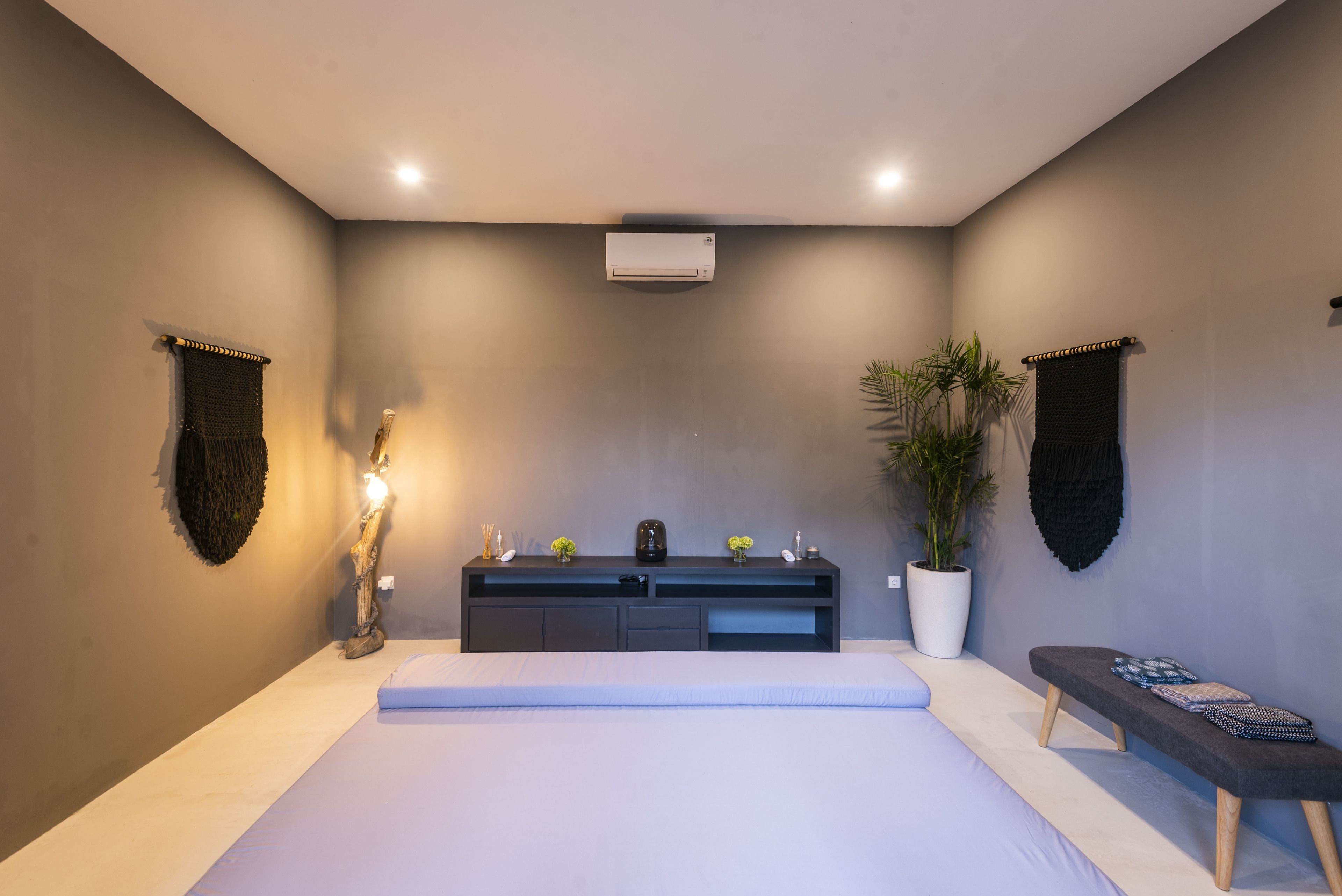 A modern bedroom with a bed, bedside table, bench, and potted plant.