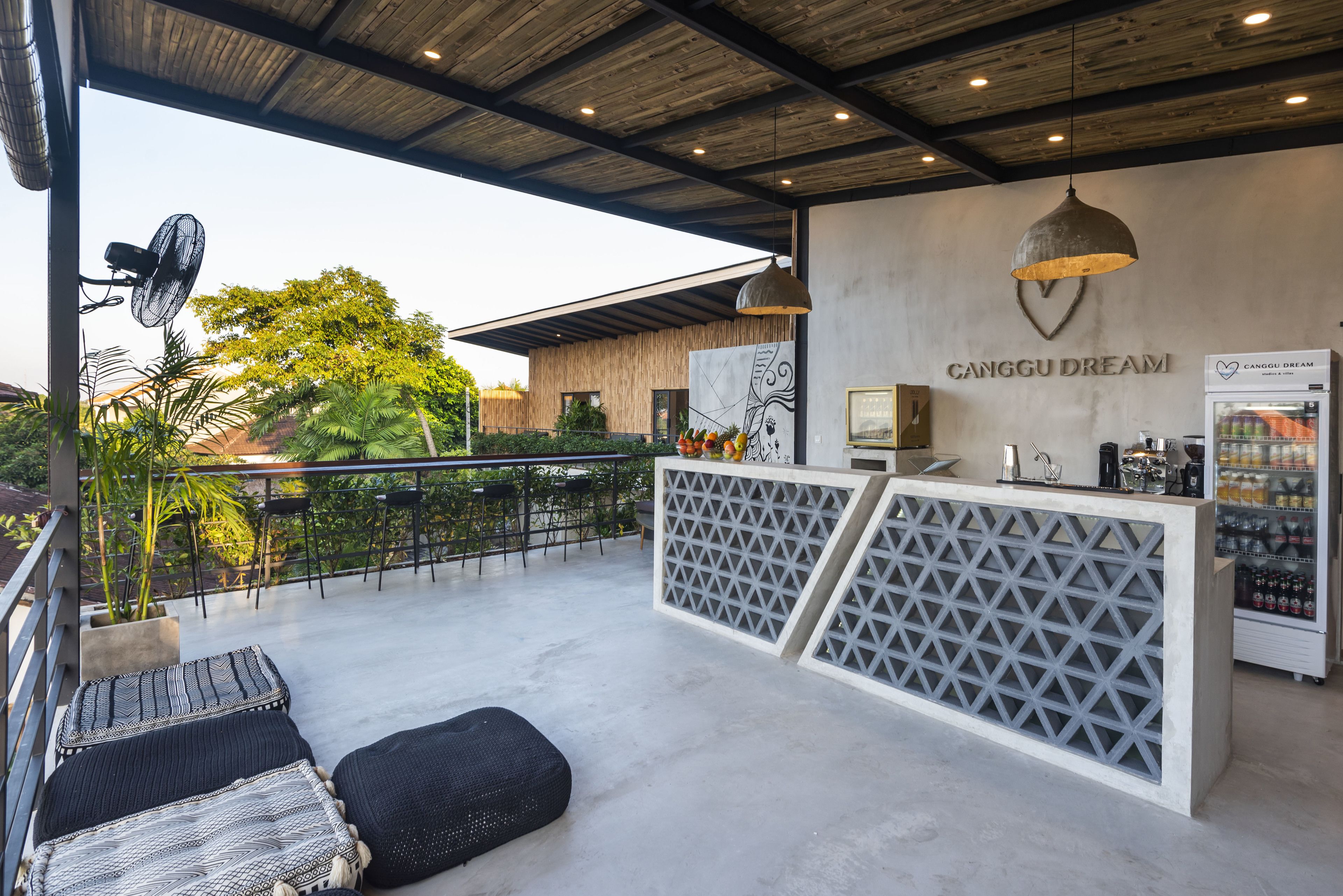 A modern outdoor seating area with a wooden ceiling, a counter with a drink dispenser, and a wall with the text "CANGGU DREAM".