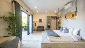 Ein modernes Schlafzimmer mit einem großen Bett, einem Schreibtisch, einem Stuhl, einer Topfpflanze und einer Glasschiebetür, die zu einem Außenbereich führt.