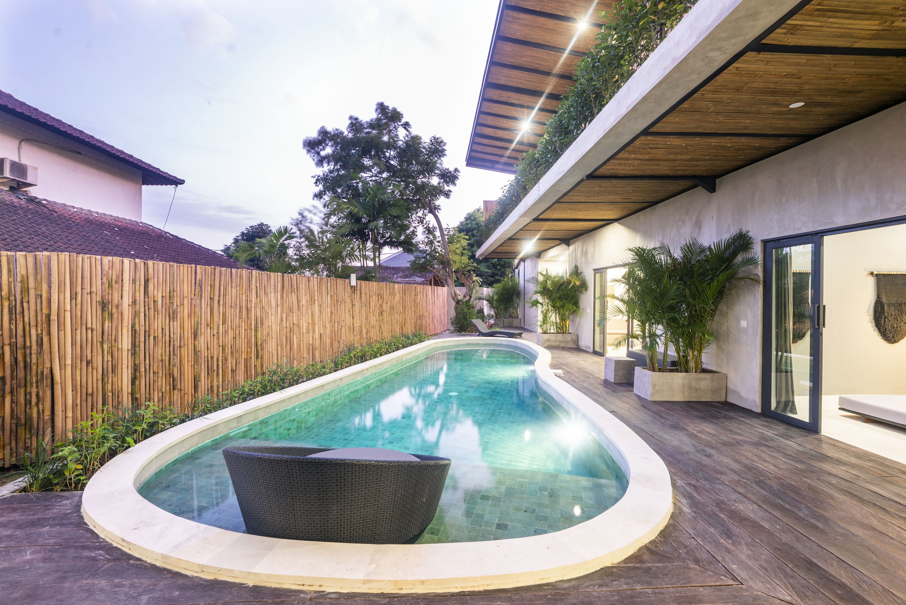 Una piscina moderna al aire libre con cubierta de madera, rodeada por una valla de bambú y plantas en macetas.