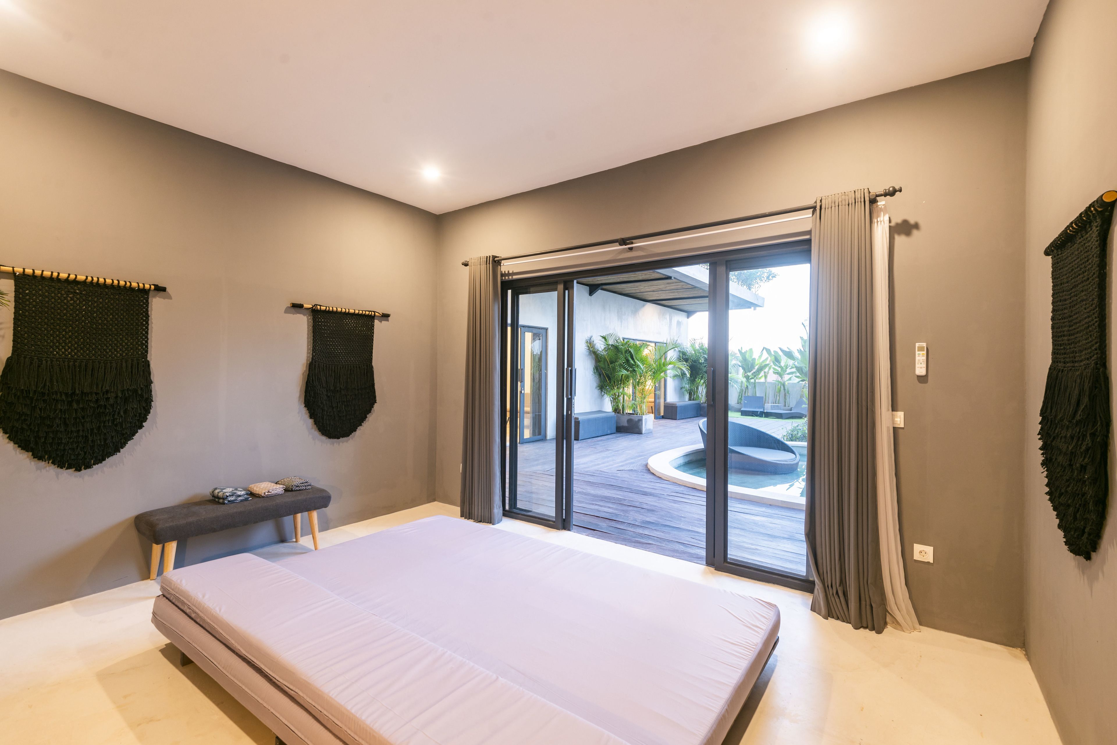Quarto com uma cama grande, um banco e vista para área externa através de uma porta de correr de vidro.