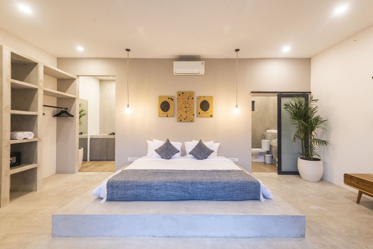 A modern bedroom with a large bed, built-in shelving, and a potted plant.