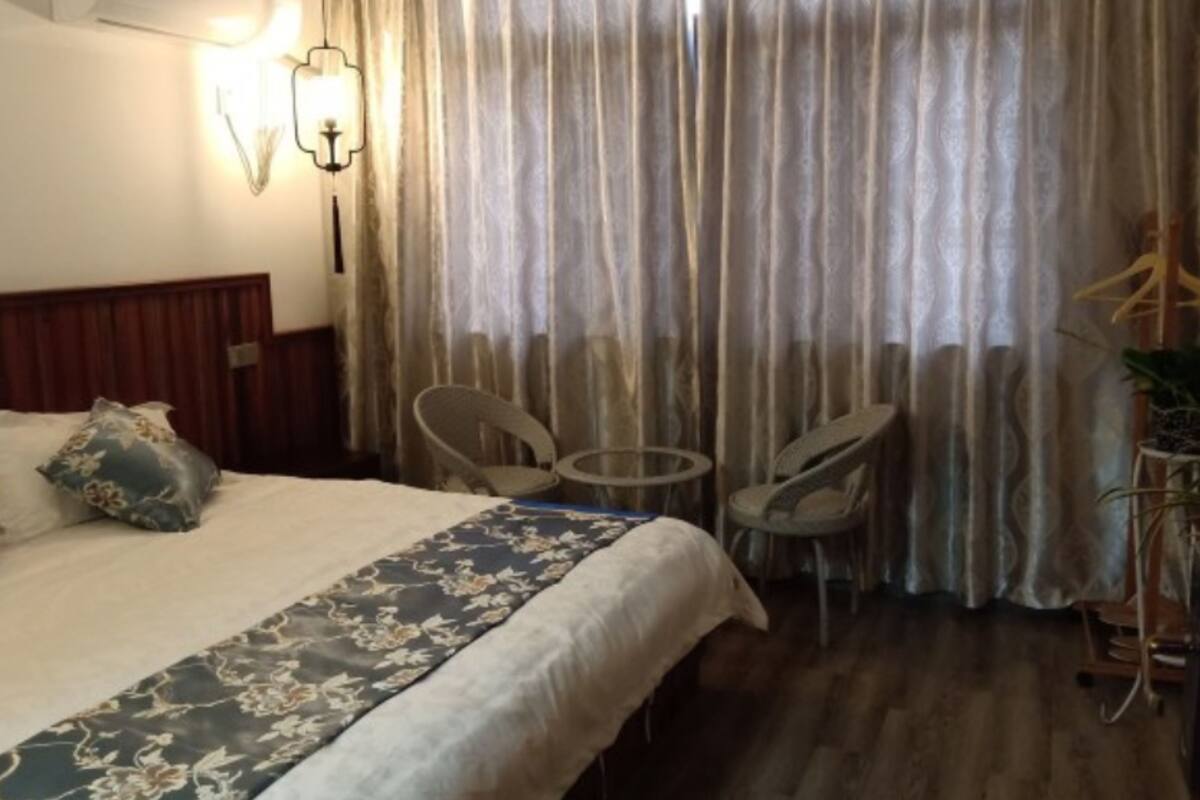 A hotel room with a bed, two chairs, a small table, a lamp, and a curtain.